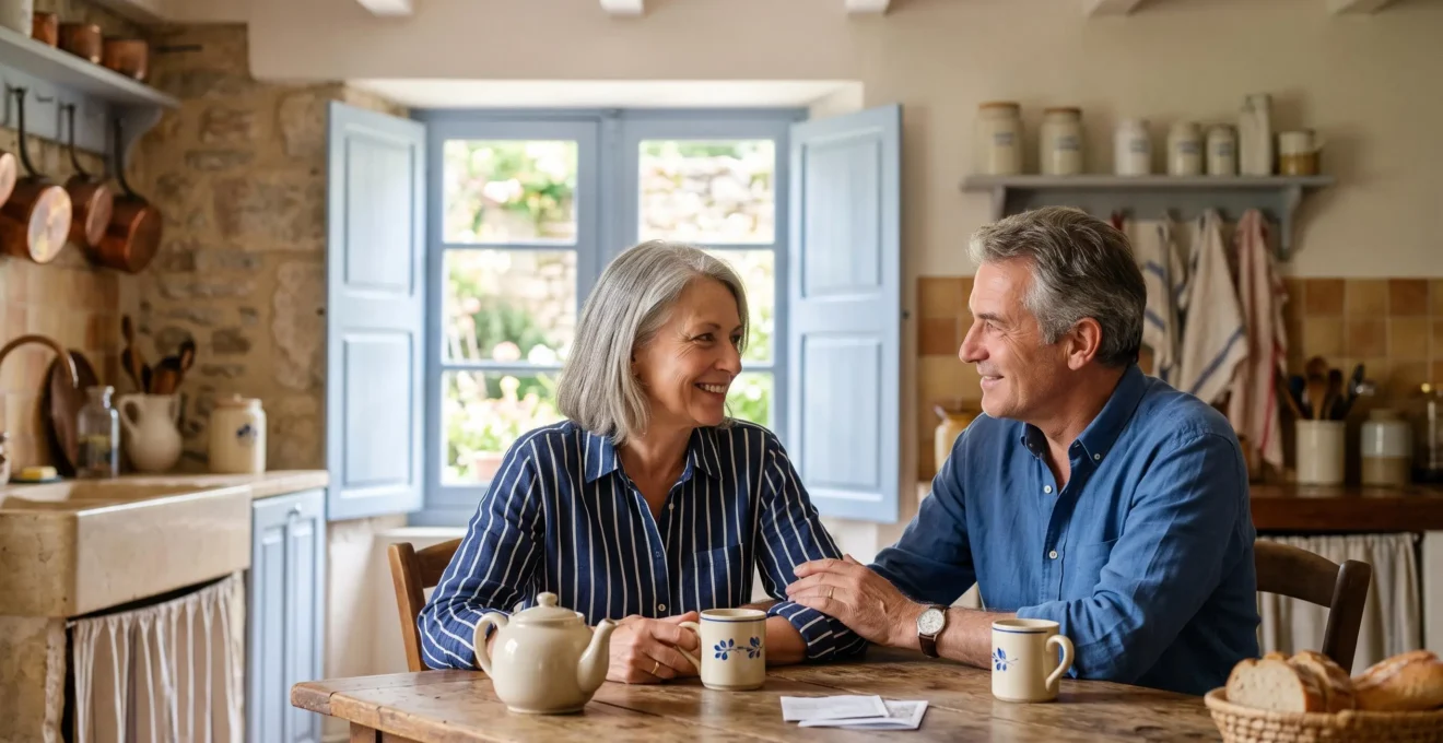 Couple de seniors français assis sereinement dans une cuisine baignée de lumière naturelle, symbolisant l'anticipation apaisée des obsèques